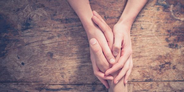 Two people holding hands in a gesture of grief support